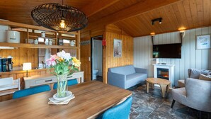 Een gezellig chaletinterieur met een houten eettafel, een bank, een televisie en een open haard.