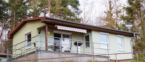 Un edificio de una planta con un porche, una pequeña zona de estar al aire libre y una escalera que conduce a la entrada.