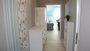 A narrow hallway with a striped wallpaper, a white dresser, and a bed with striped bedding in the background.