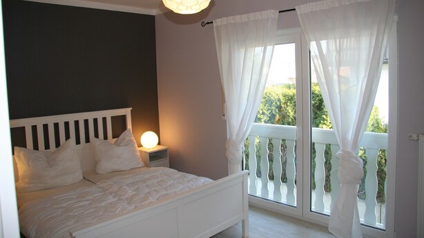 A bedroom with a bed, bedside table, and a window with curtains.