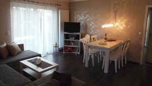 A living room with a sofa, a dining table with chairs, a TV on a stand, and a wall with a floral pattern.