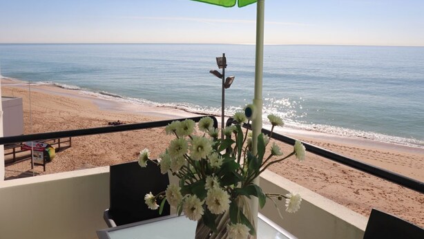 Un balcone con un ombrellone verde, un vaso di fiori e vista sulla spiaggia e sull'oceano.