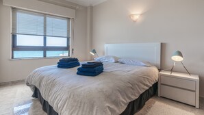 Un letto rifatto con asciugamani piegati, una lampada da comodino e vista sul mare attraverso una finestra.