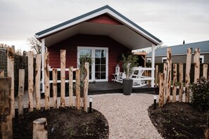 Une cabane en bois rouge, avec un porche blanc, un toit noir et un chemin de gravier menant à l’entrée.
