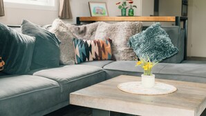 Ein modernes Wohnzimmer mit einem grauen Sofa, einem Holztisch mit Blumenvase und einer farbenfrohen Decke.