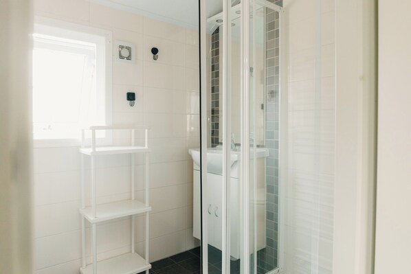 Une salle de bain avec une douche à parois de verre, un lavabo blanc et une étagère blanche.