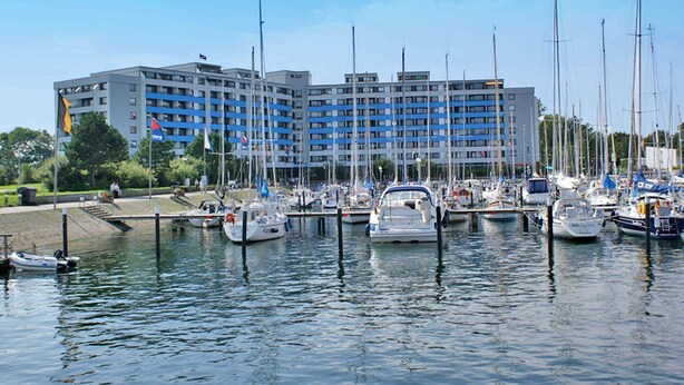 A marina with multiple boats docked in front of a large hotel with a modern architectural design.
