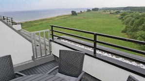 A balcony with a view of the sea, a grassy field, and a chair.