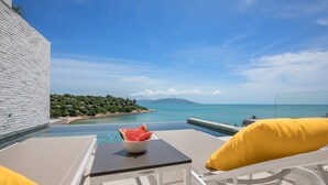 Ein Poolbereich mit Blick auf das Meer, ein weißes Gebäude und ein Tisch mit einer Schüssel Wassermelone.