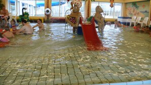 Un espace de jeux aquatiques avec des toboggans et une piscine, entouré de palmiers et agrémenté d’une fresque murale.