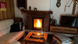 Un salon chaleureux avec une cheminée, un canapé, une table basse sur laquelle repose un verre de vin et un téléviseur.