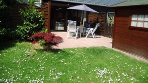 Une terrasse avec une table et des chaises, entourée d’une pelouse parsemée de fleurs blanches.