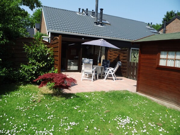 Eine Terrasse mit Tisch und Stühlen, umgeben von einer Rasenfläche mit weißen Blumen.