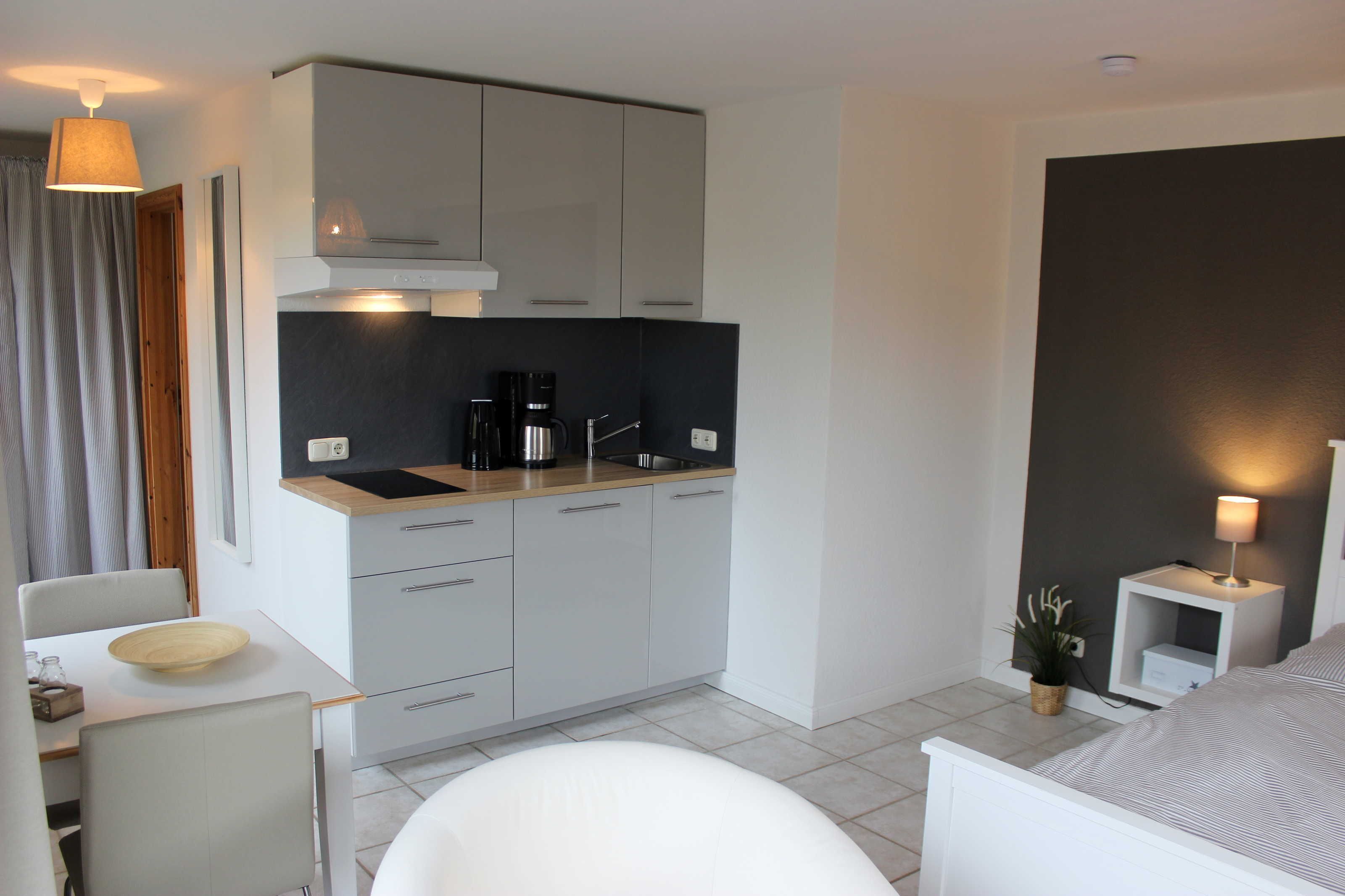 A modern kitchen with grey cabinets, a coffee maker, and a small dining area with a white table and chairs.