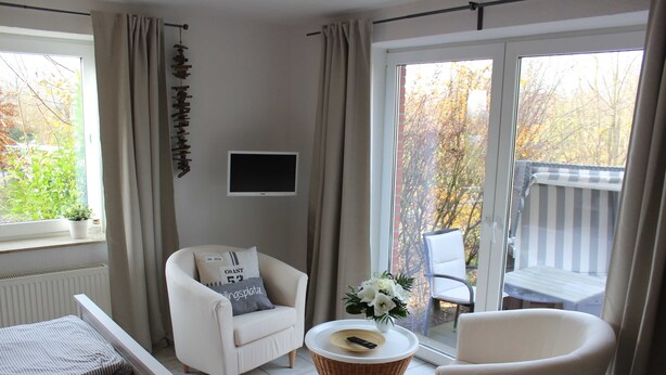 A modern living room with a sofa, a chair, a small table with a vase of flowers, and a television on the wall. - Vacation apartment Matrosennest - OSTSEE-Ferienwohnungen (Hasselberg)