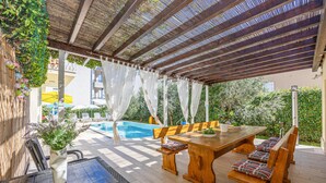 An outdoor patio with a pool, wooden furniture, and a pergola with a mesh roof. - Beautiful home in Kastel Stafilic with sauna (Kastel Stafilic)