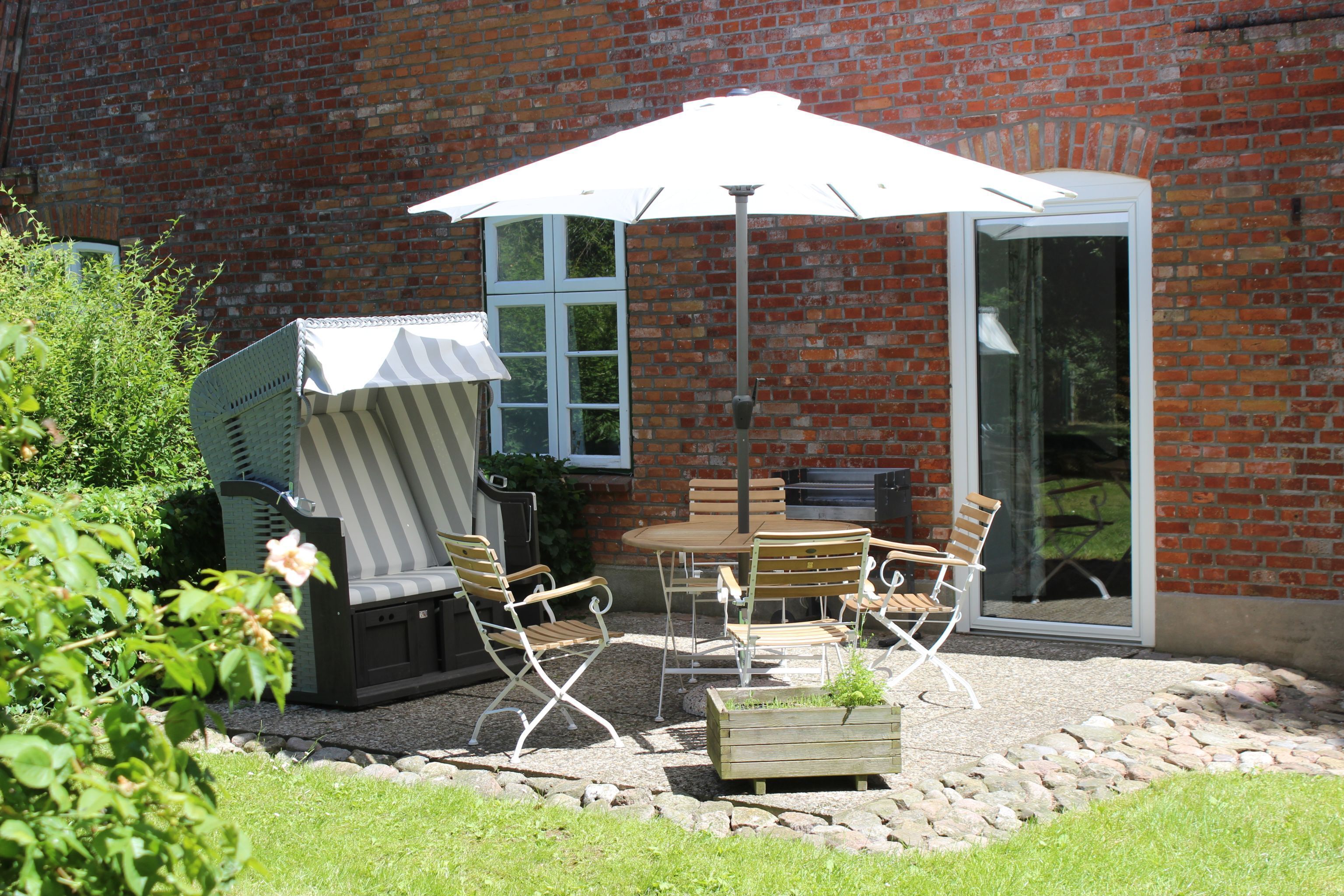 Eine Terrasse mit Tisch und Stühlen, einem überdachten Grill und einer Ziegelwand.