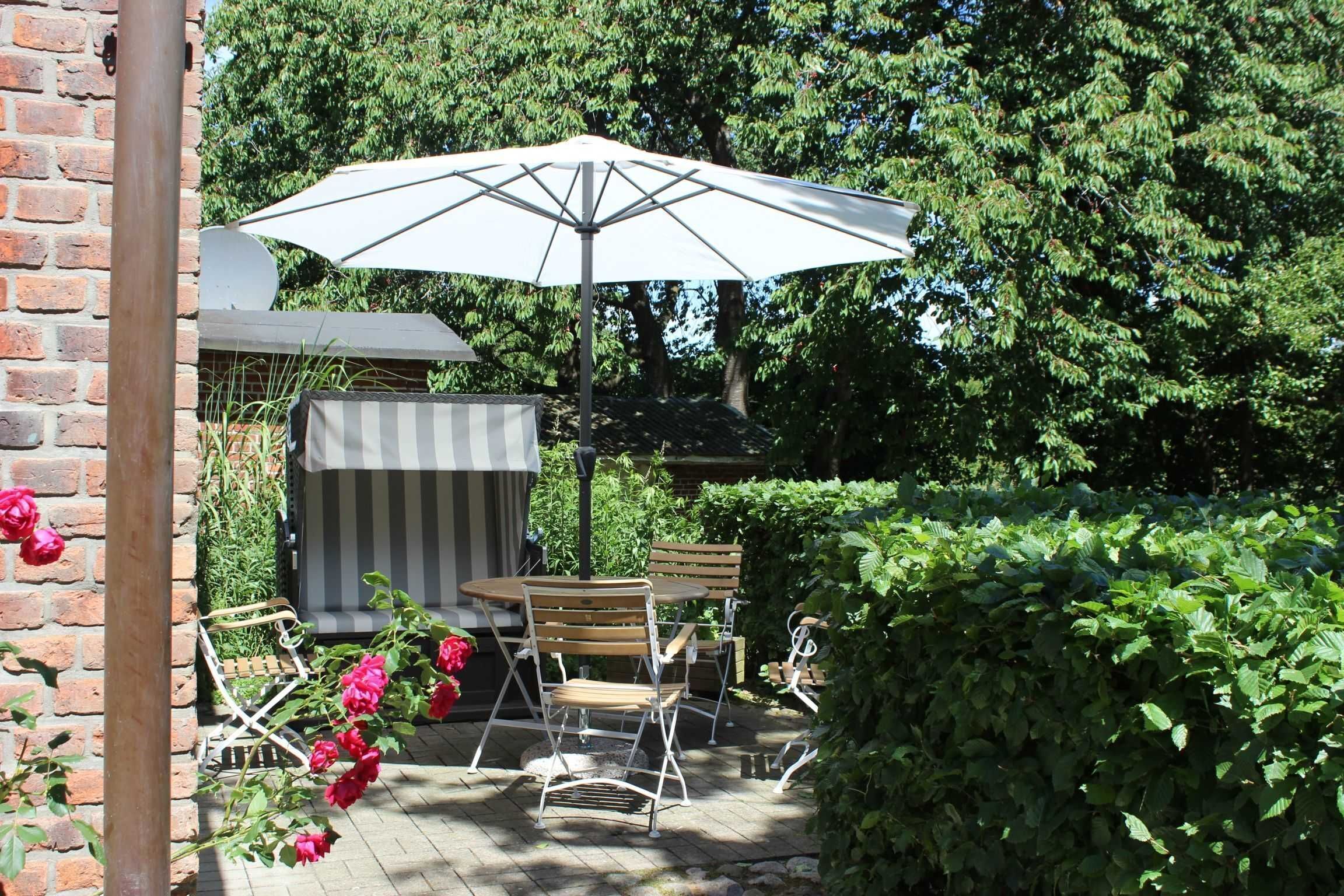 Une terrasse extérieure avec une table et des chaises, un grand parasol et un mur en briques.