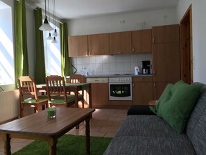 Une cuisine compacte avec des meubles en bois, une table à manger avec des chaises, un canapé et une petite fenêtre avec des rideaux.