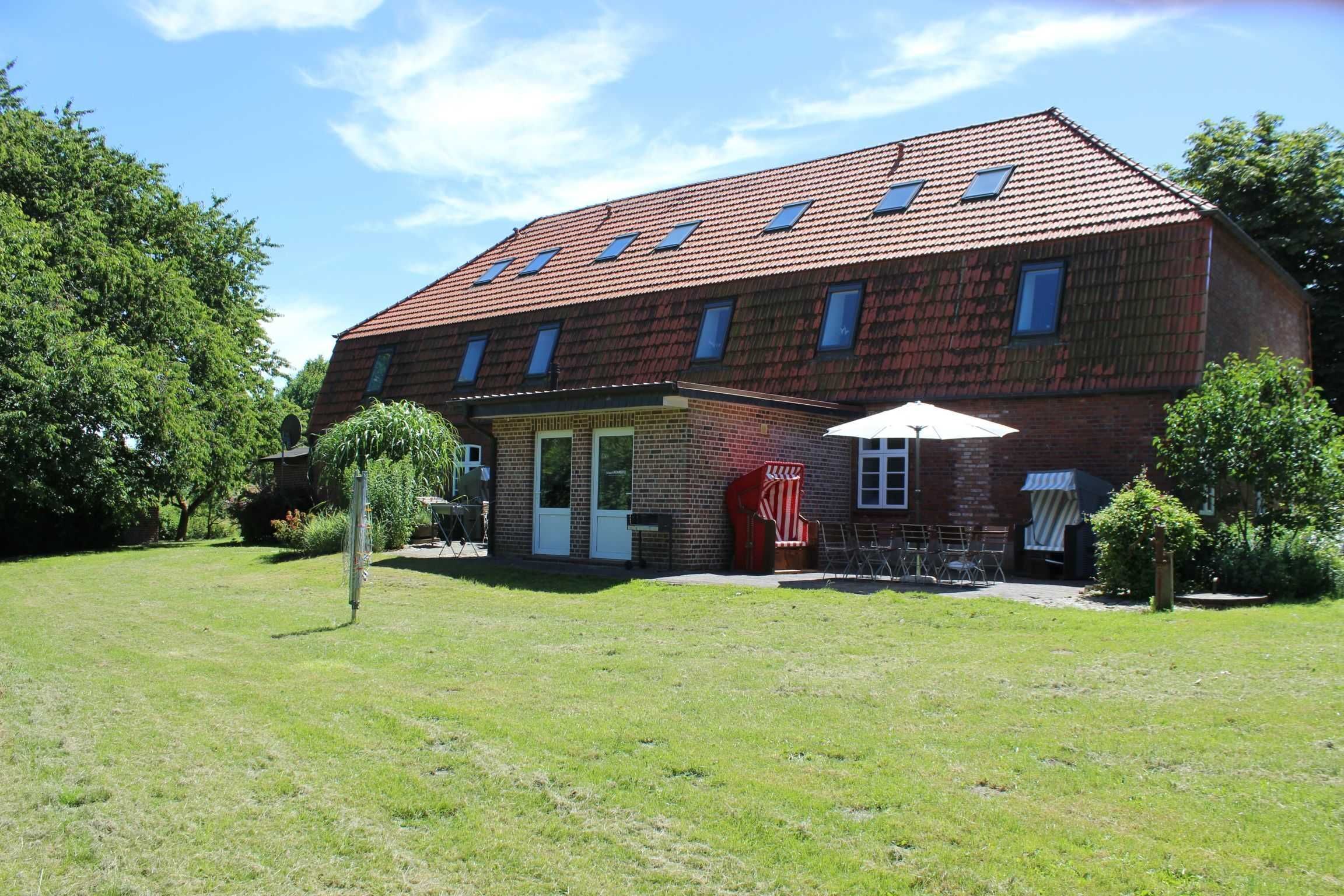 A two-story house with a red-tiled roof, a brick exterior, and a small front porch with a red chair and umbrella.