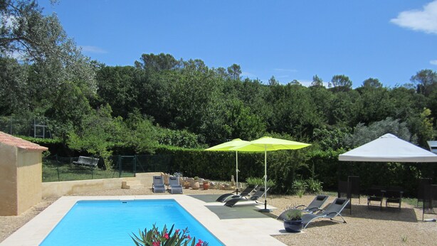 Ein Swimmingpool mit Liegestühlen und Sonnenschirmen, umgeben von einem Garten und Bäumen.
