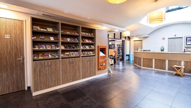 A hotel lobby with a reception desk, wooden bookshelves, and a tiled floor. - Wilbrink 6 to 8-person bungalow (Voorthuizen)