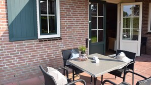 A patio with a table and chairs, a potted plant, and a door leading to a covered area. - Wilbrink 6 to 8-person bungalow (Voorthuizen)