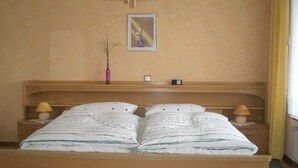Habitación de hotel con una cama de madera, dos mesitas de noche con lámparas, un cuadro enmarcado en la pared y un florero sobre una de las mesitas.