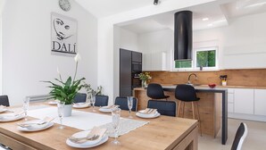 A modern dining area with a wooden table set for four, a potted plant, and a wall clock. - Awesome home in Kujici with sauna (Kujici)