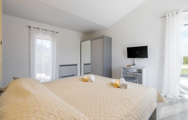 Habitación de hotel con cama, escritorio, televisor de pantalla plana, espejo y ventana con cortinas.