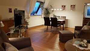 Een woonkamer met een televisie, een eettafel, stoelen en een bank.