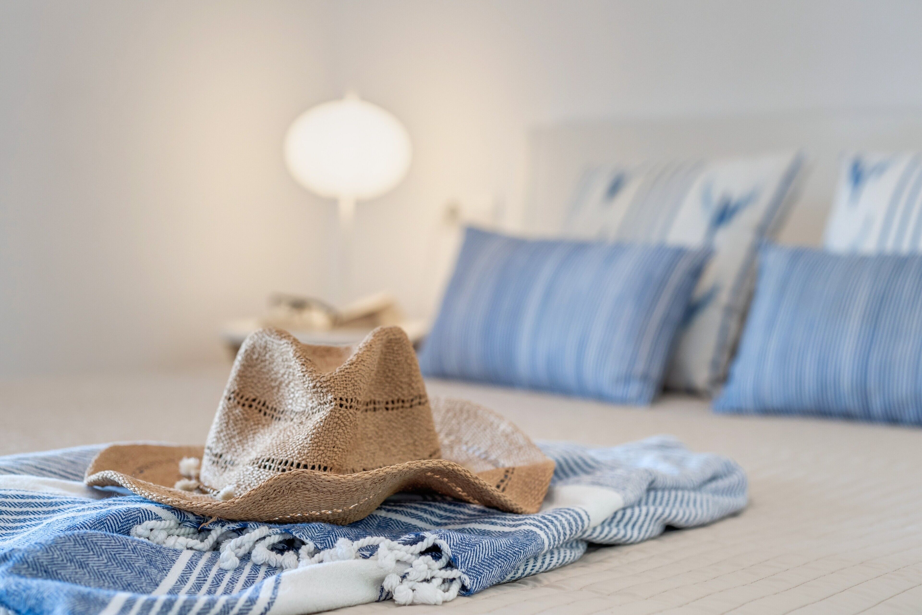 Un lit avec une couverture à rayures bleues et blanches, un chapeau de paille et des oreillers bleus.