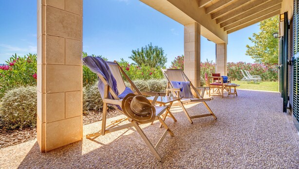 Un patio exterior con sillones, una mesa y un área cubierta con una pérgola.