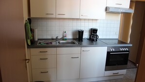 Uma cozinha compacta com armários brancos, pia de aço inoxidável, cafeteira e forno embutido.