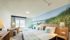 A hotel room with a bed, desk, chair, and a view of the ocean.