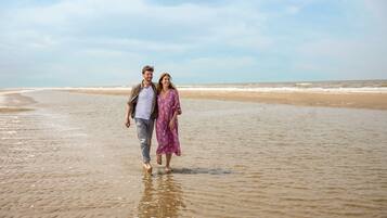 Um casal caminhando numa praia sob um céu claro.