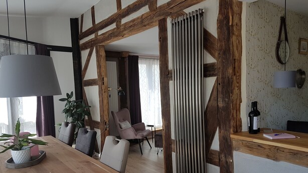 A dining area with a wooden table, chairs, and a potted plant. There is a radiator on the wall and a hanging lamp. - Apartment Rose       (Obermöllrich)