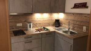 Una cocina moderna con armarios grises, encimera de madera, una tetera, una cafetera y un letrero en la pared.