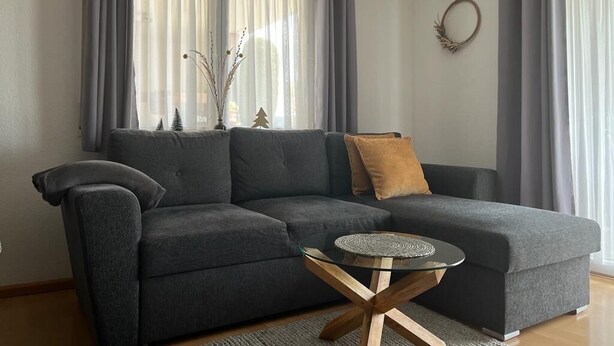 Una sala de estar moderna con un sofá seccional gris, una mesa de centro de vidrio y un adorno circular en la pared.
