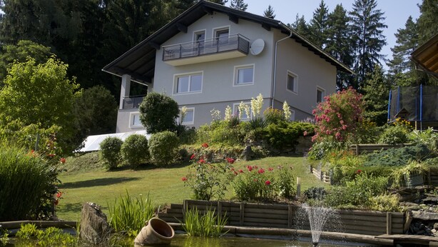 A two-story house with a balcony, surrounded by a garden with various plants and flowers. - Holiday house on the outskirts of Klagenfurt with a wonderful view (Klagenfurt am Wörthersee)