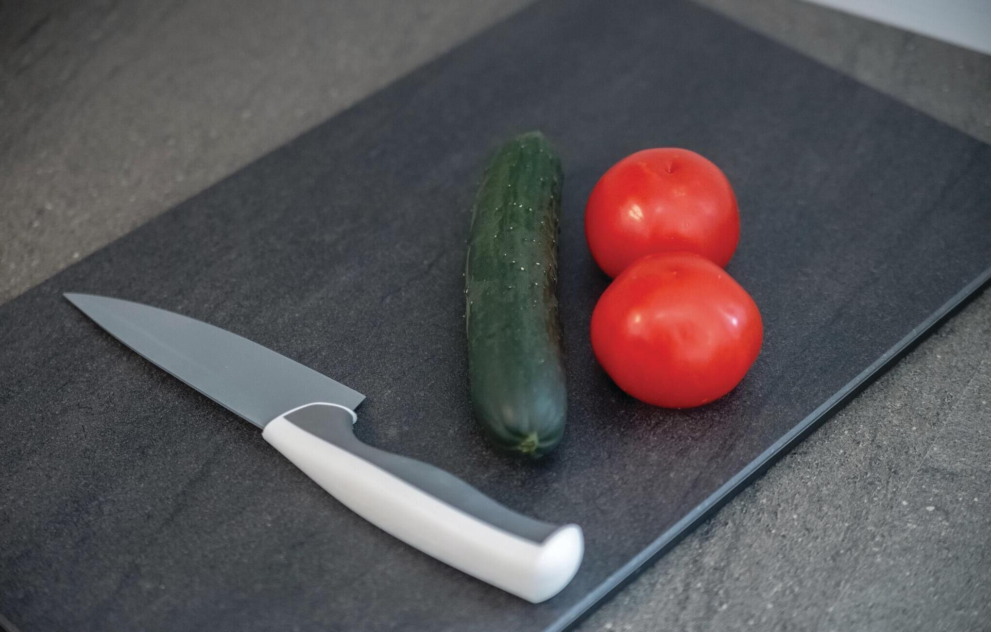 A cutting board with a knife, a cucumber, and two tomatoes.