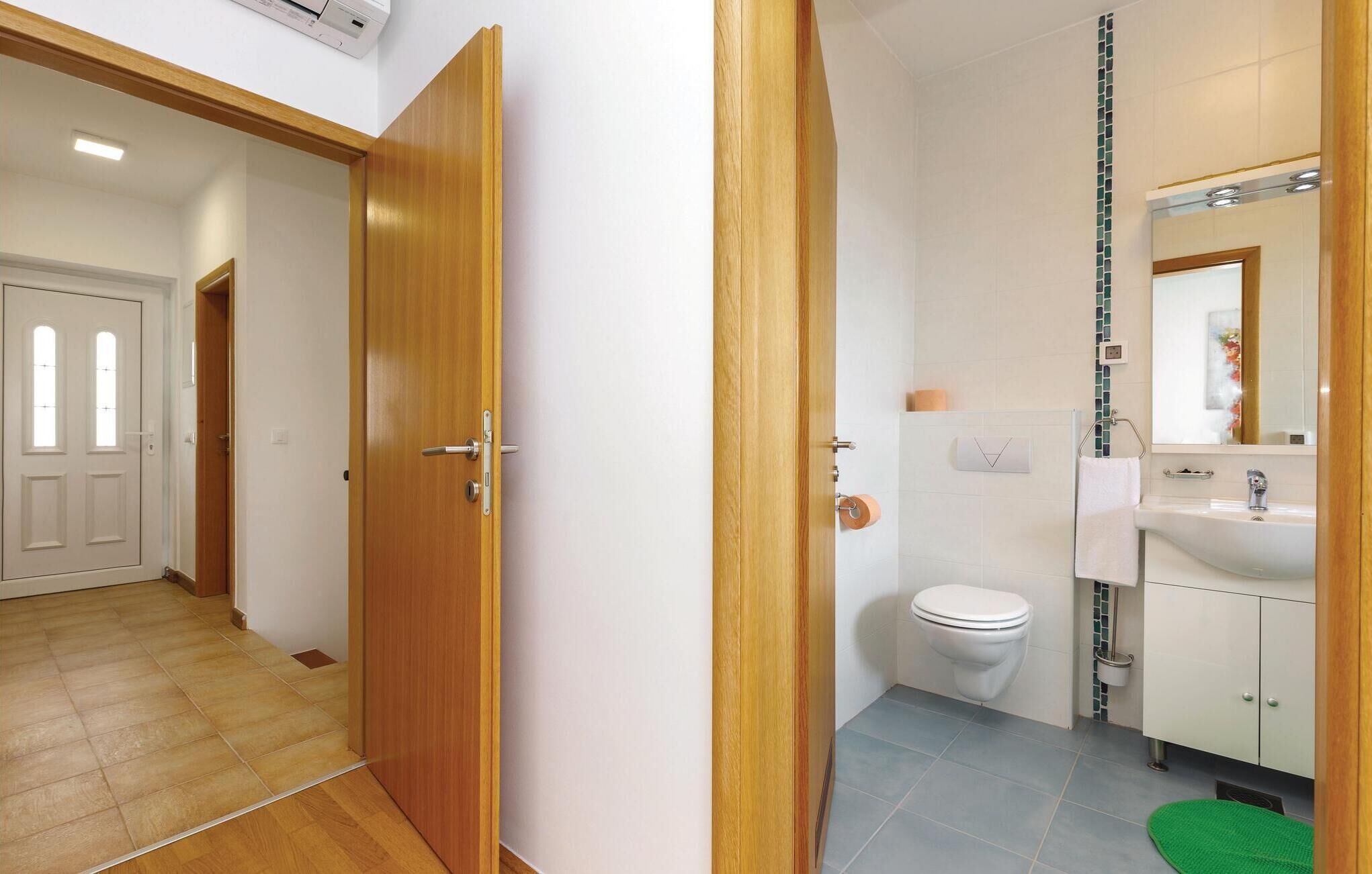 A hallway leading to a bathroom with a toilet, sink, and mirror.
