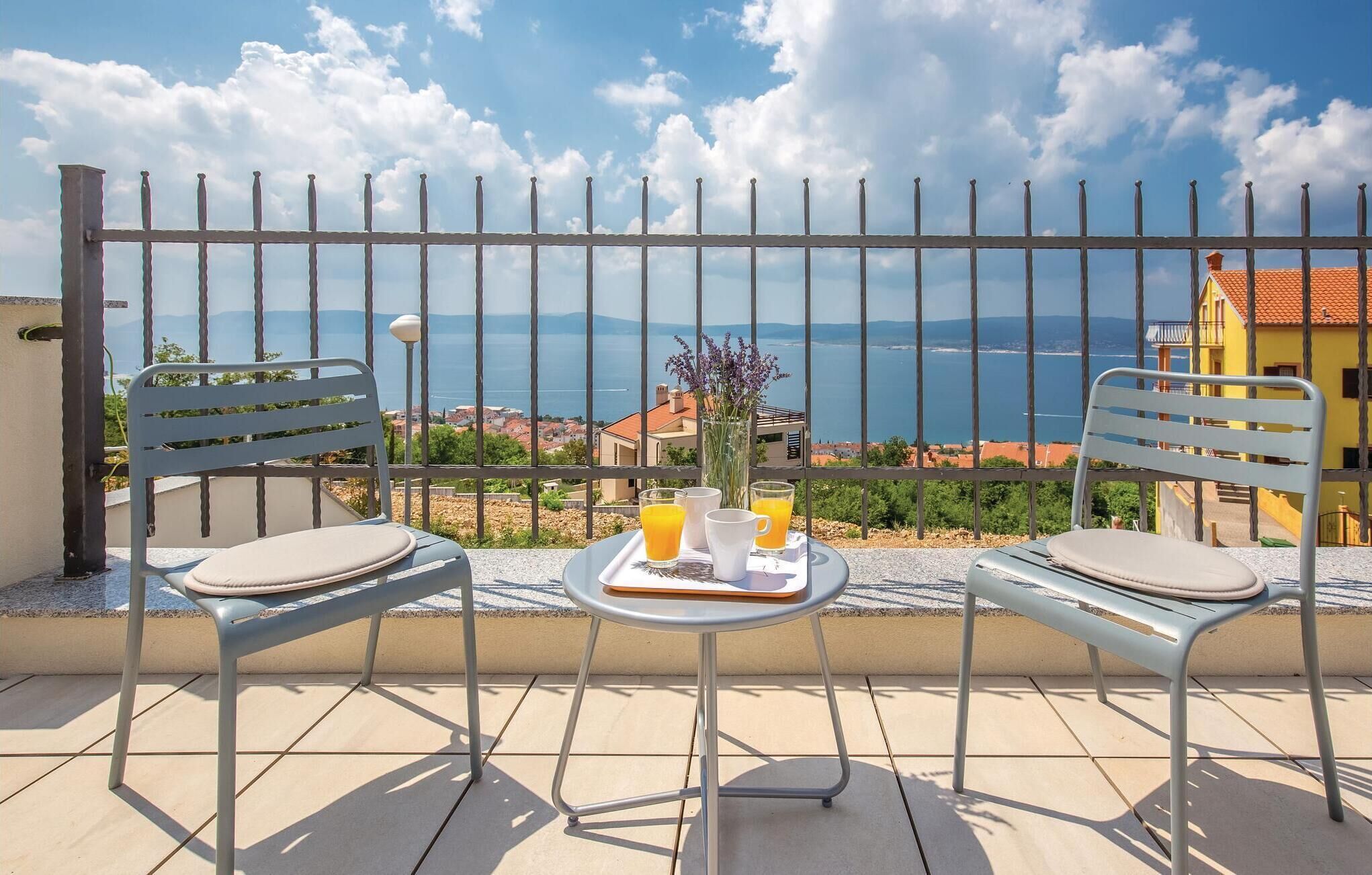 A balcony with two chairs and a table, a vase with flowers, and a tray with orange juice and a cup.