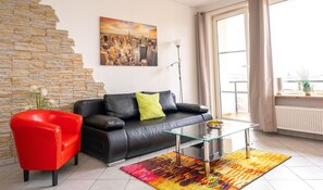 A living room with a black leather sofa, a red chair, a glass coffee table, and a colorful rug. - ACS 9 - Art City-Studio Kassel 9 (Niestetal)