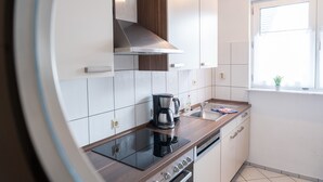 Una cuina moderna amb armaris blancs, una campana extractora d'acer inoxidable, una placa d'inducció negra i un forn integrat.