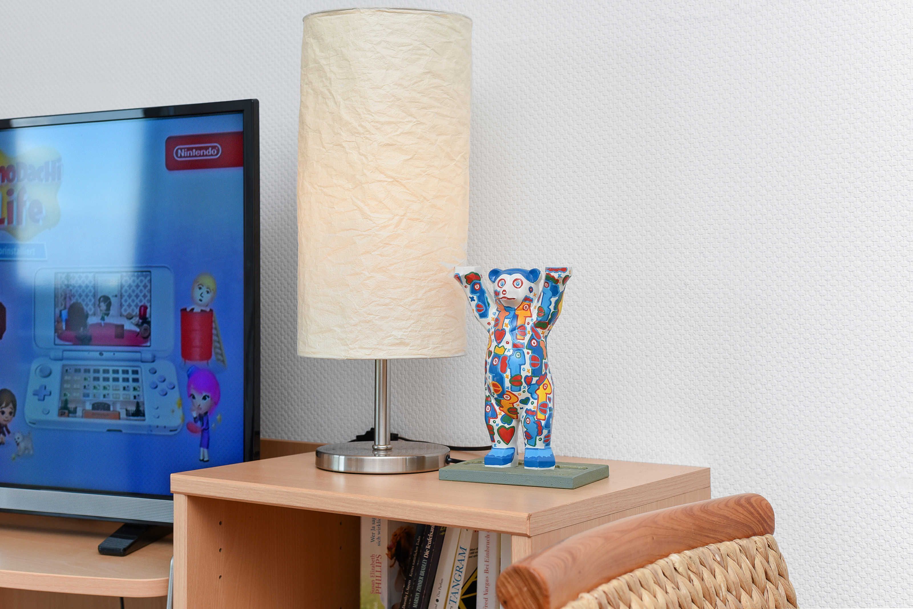 A television displaying a Nintendo game, a lamp, and a colorful figurine on a wooden shelf.