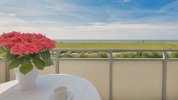 Un balcon avec une table blanche, une tasse blanche et un vase rempli de fleurs roses.