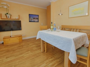 A dining area with a table set for two, a television mounted on the wall, and a framed picture above the table. - N26 (BC.a5) - Stranddomicil Steiner (Büsum)