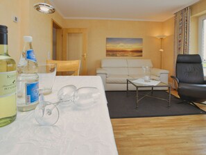 A hotel room with a wooden floor, a white sofa, a black leather chair, a glass coffee table, and a painting of a sunset on the wall.