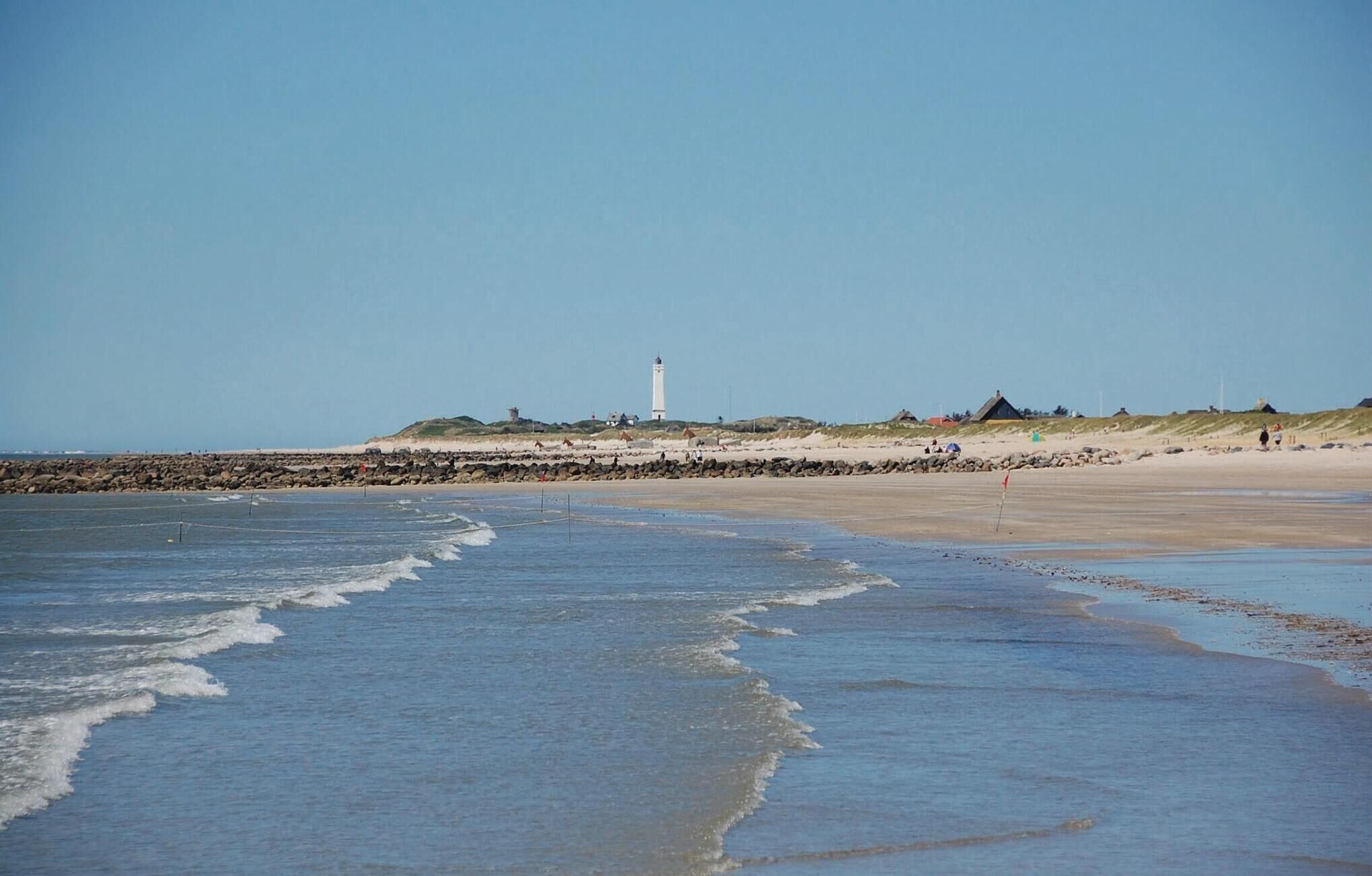 A beach with a lighthouse, rocky shoreline, and a sandy area with people.